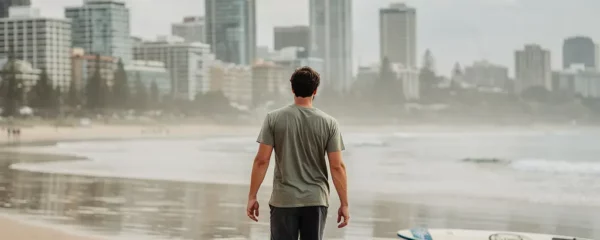 Jeune adulte marchant sur une plage australienne avec skyline urbaine en arrière-plan
